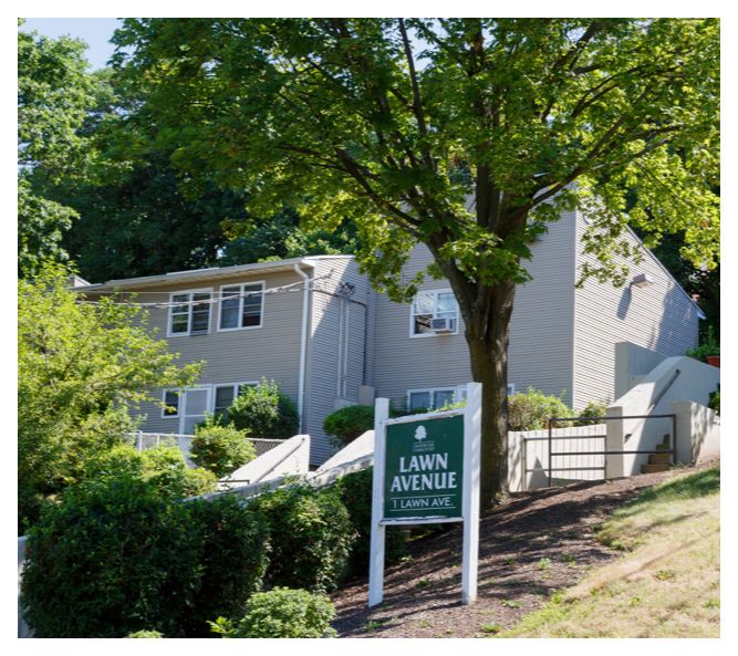 The well-maintained townhouse buildings are surrounded by trees and shrubbery. An AC unit peeks out of a window.