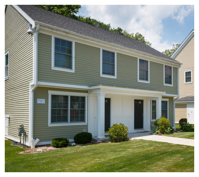 Small shrubs and flowers line the entrance to this Colonial-style housing unit, which is surrounded by a manicured lawn.