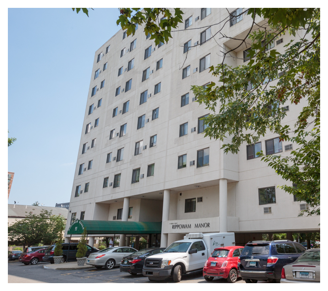 This modern senior-living property is nine stories and constructed of smooth concrete. An awning extends from the doorway.