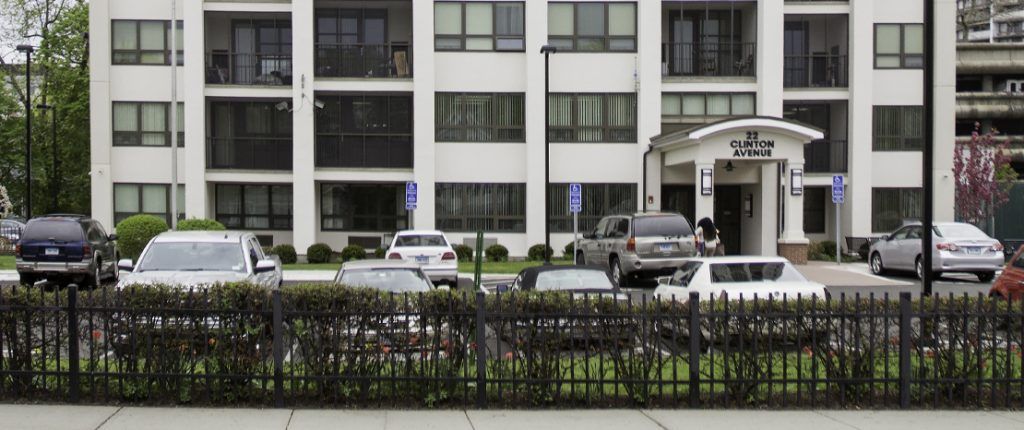 Surrounded by a metal fence and shrubbery, Clinton Manor has a dedicated outdoor parking lot with handicap parking spaces.