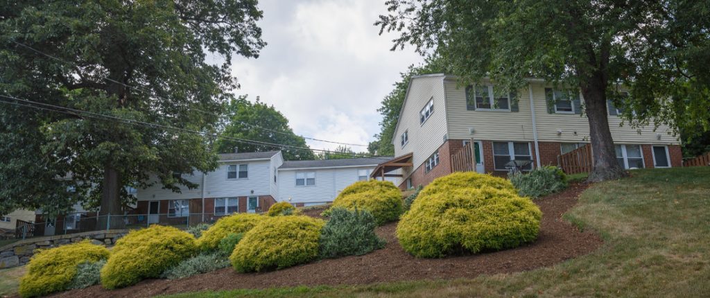 A view of the housing units also features the landscaped shrubbery, tall trees, stone walls, and plenty of greenery.