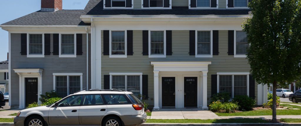 This Colonial-style building features many windows, private entrances, and is surrounded by a sidewalk and greenery.