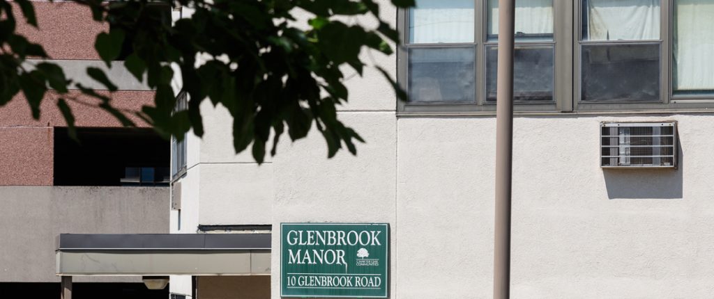 A horizontal view of the Glenbrook Manor sign also shows the row of an apartment's windows and the in-wall AC unit.