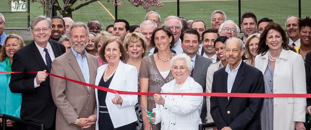 A group of well-dressed people stand proudly, ready to cut the red ribbon and open Greenfield.