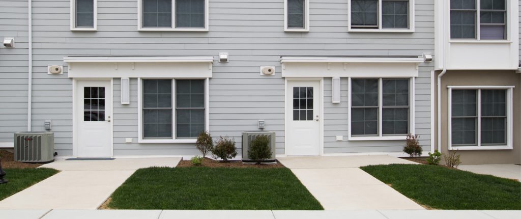 Sidewalks lead to the ground-level, rear, private entrances complete with outdoor lighting, a patch of grass, and shrubbery.