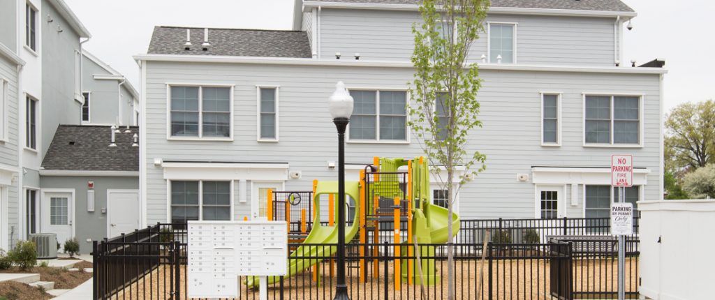 The gated, communal playground is right next to the secure mailboxes and nestled by some of the buildings.