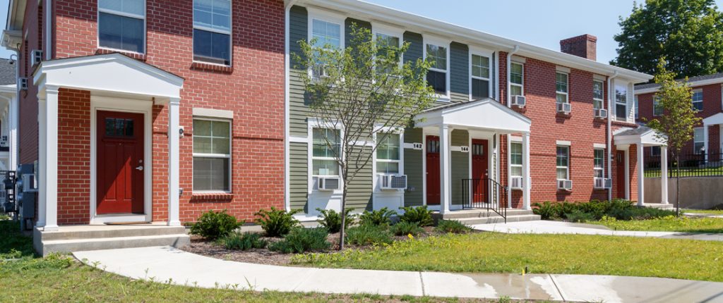 Sidewalks lead to covered entrances and brightly colored doors. The exterior has a contemporary mix of brick and siding.