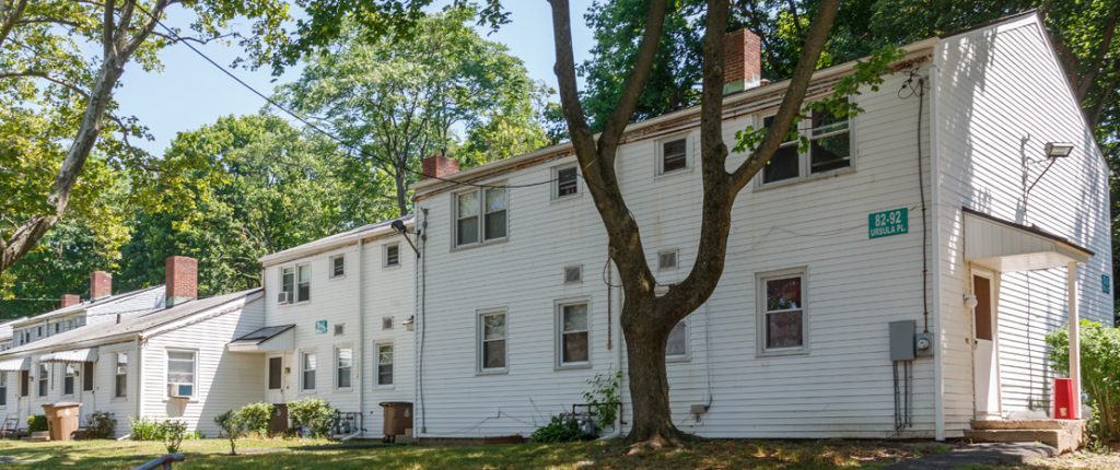 A view from behind shows green grass, many windows, some with window AC units, covered entrances, and exterior lighting.