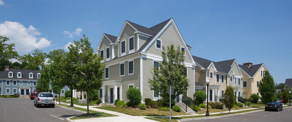 A wide view shows indented parking and a community of new-looking buildings surrounded by plants and shrubbery.