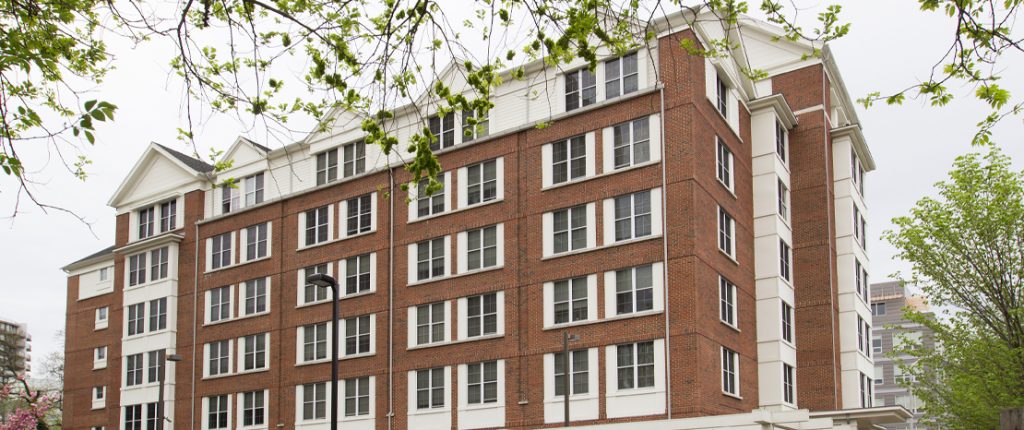 Looking through the trees at the mixed-brick, six-story Post House and its inviting white accents.