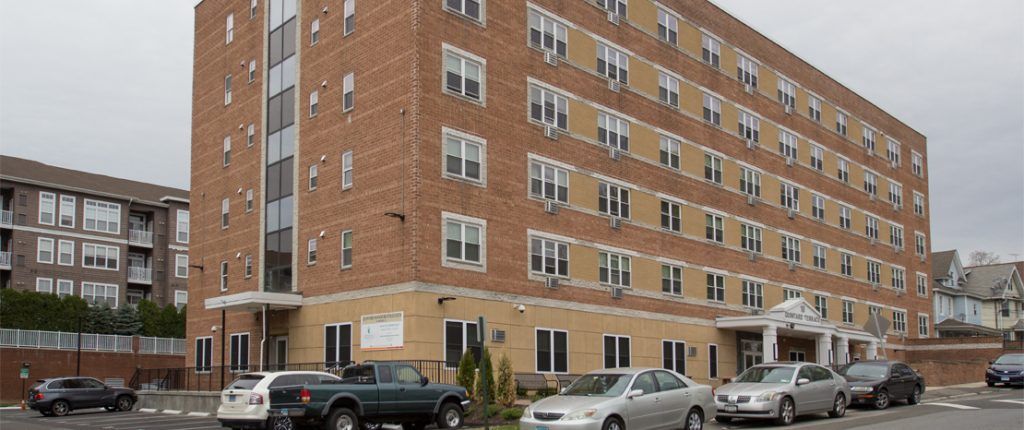 Quintard Terrace stretches horizontally showcasing the many windows and in-wall AC units. There is a parking lot to the left.