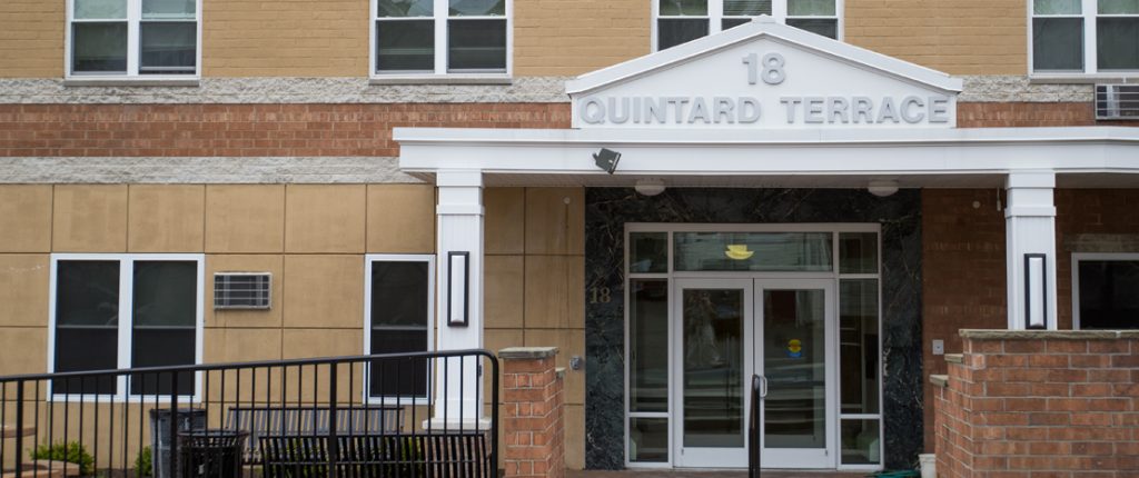 The covered front entrance to this senior-living property is well-lit and has outdoor benches.