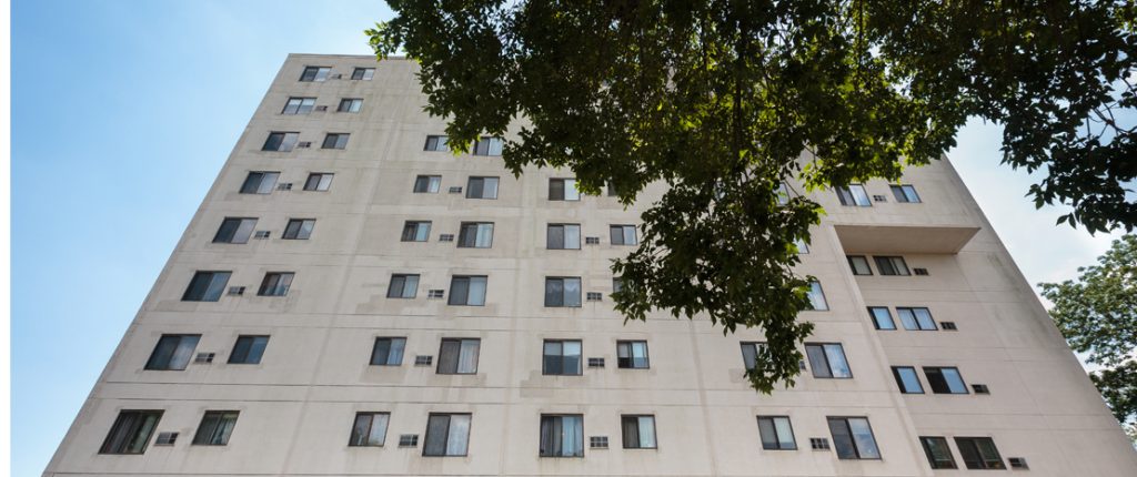 Looking through a tree at the senior-living property that features vertical sliding windows and a smooth concrete facade.