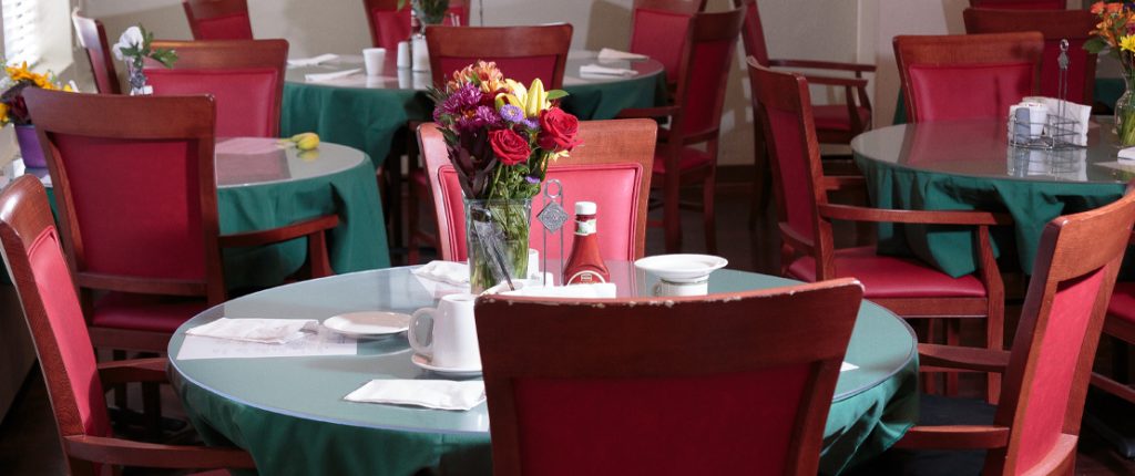 The dining area features many cloth-covered tables adorned with fresh flowers. Surrounding the tables are cushioned chairs.