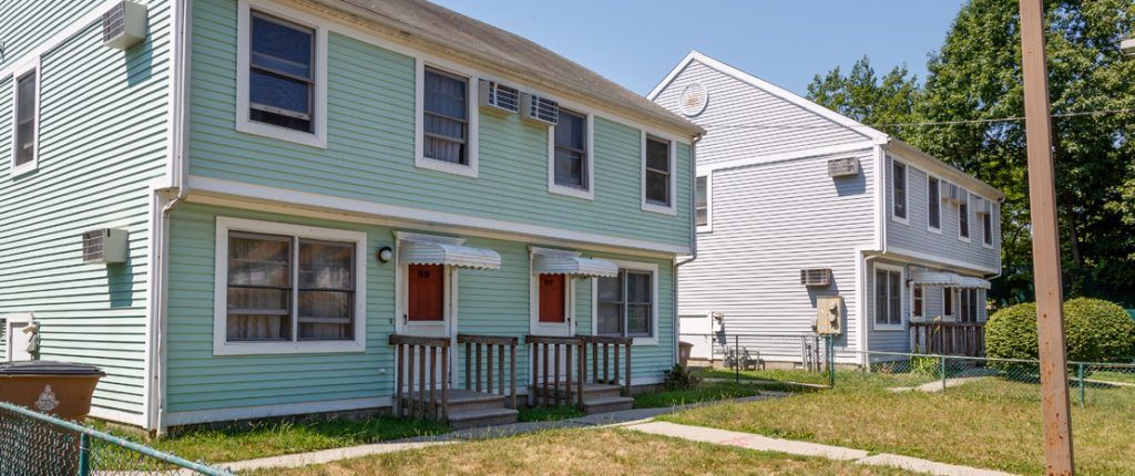 The housing unit sits in the sunl the siding looks clean and well-maintained. There are multiple in-wall AC units installed.