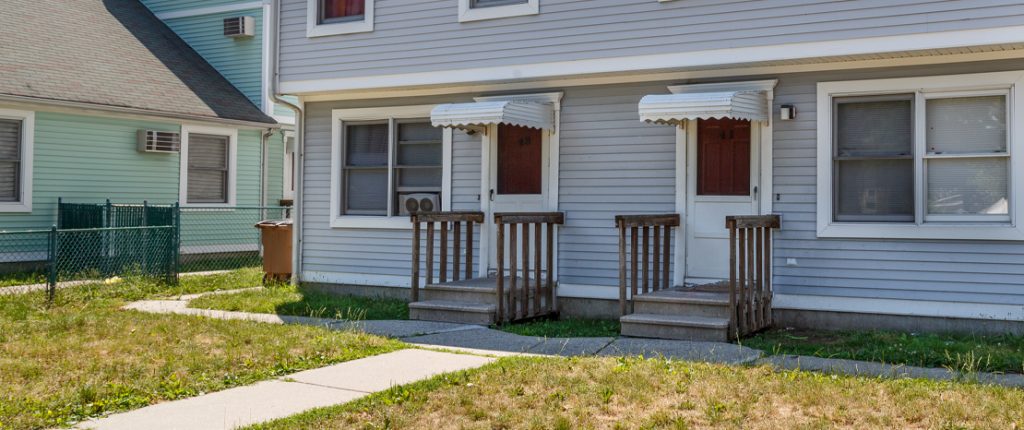 A sidewalk goes from the street to the private entrances and wraps around towards the back. A fence separates the buildings.