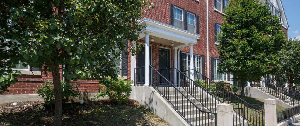 The private, front entrances have porch lights above each door. Small trees line the sides of the stairs to the entrances.