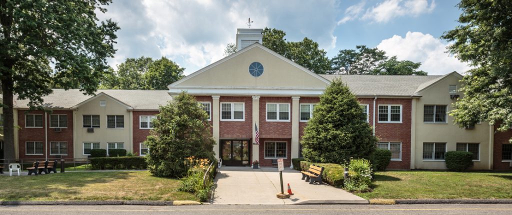 Wormser Congregate is a stately building with plenty of windows and outdoor seating among the grass, flowers, and shrubbery.