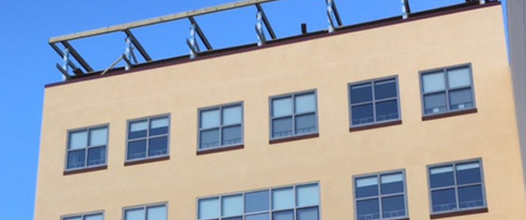 Looking up to the top of the building shows the many windows and a glimpse of the rooftop patio framework.