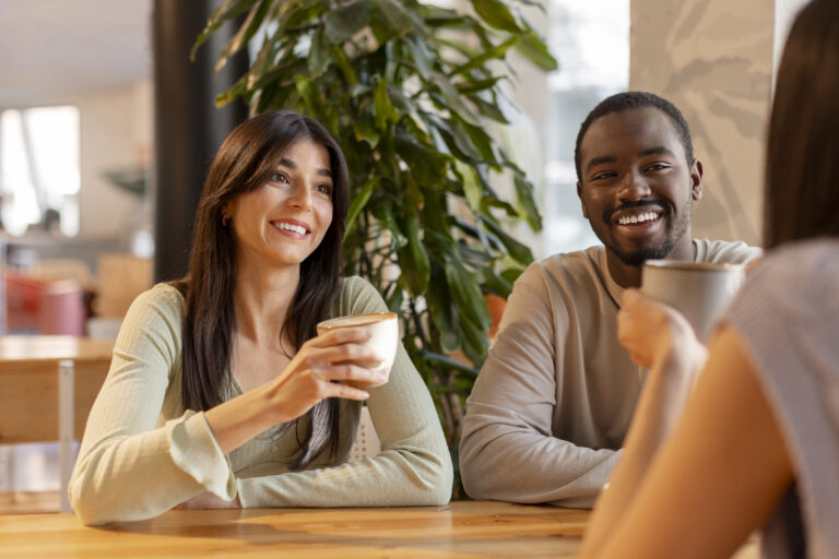 A small group of people sit together over coffee, smiling and talking in a bright, comfortable space.