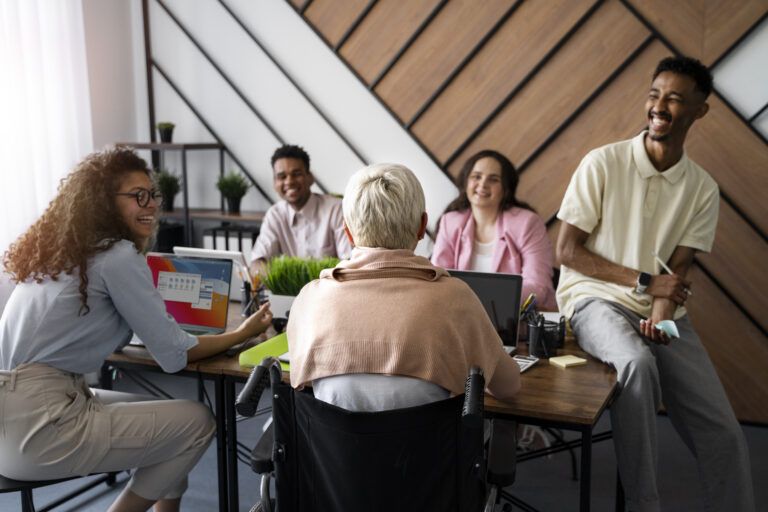 Group of adults smiling and talking together around a table in a bright room.