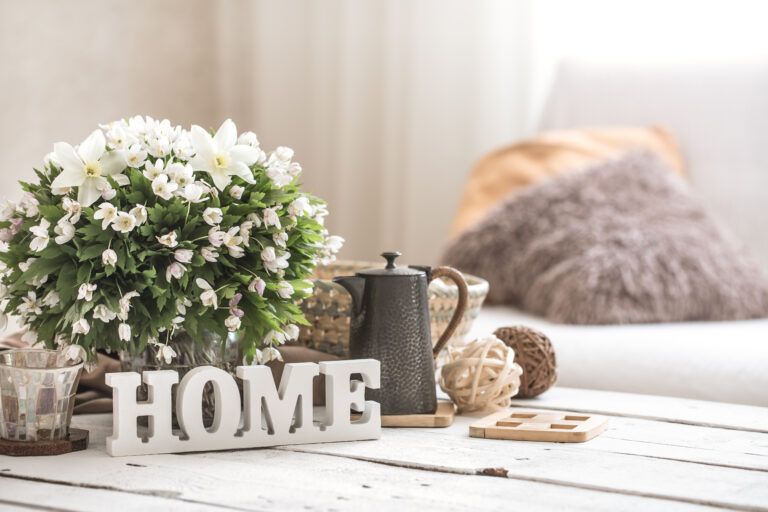 A cozy living room with natural light, a bouquet of white flowers, a teapot, and soft pillows.