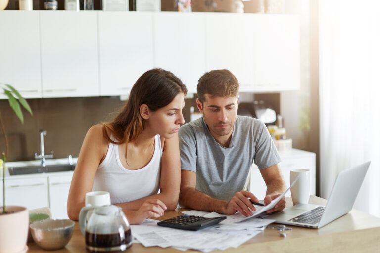 A man and woman sitting at their kitchen table reviewing bills and expenses while planning their monthly budget.
