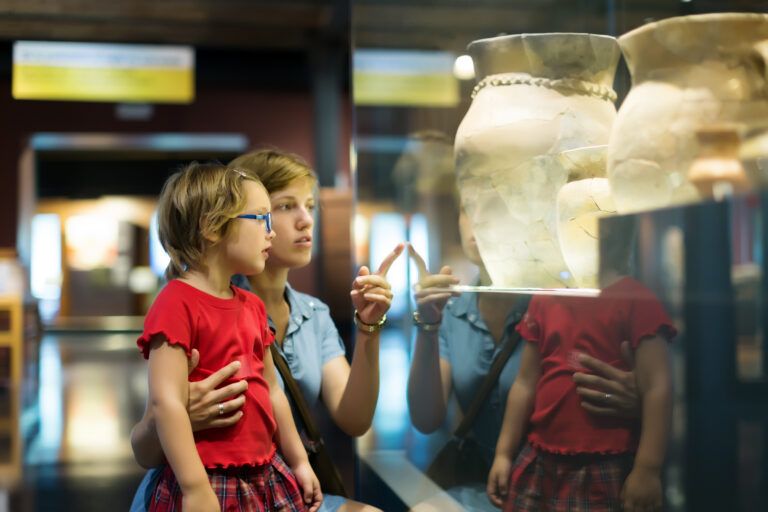 Adult and child standing in a museum gallery, looking at ceramic vessels displayed behind glass.